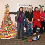 Secretary Ross and DMS employees pose near a tree made of canned goods encircled by a toy train